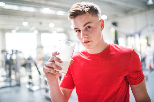 A young fit men in crossfit gym holding a glass with protein drink. Copy space.