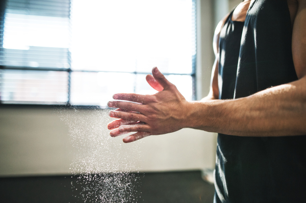 Fit young bodybuilder in gym smears his hands with magnesium. Close up. Copy space.