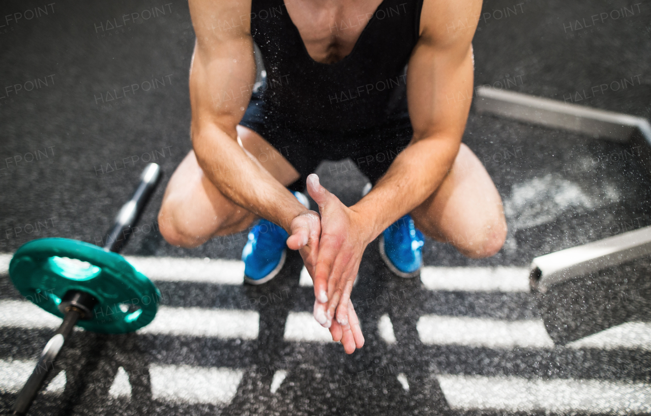 Unrecognizable fit young man in gym with barbells smearing his hands with magnesium.