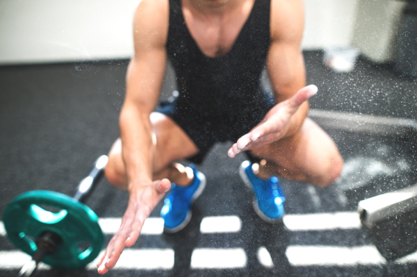 Unrecognizable fit young man in gym with barbells smearing his hands with magnesium.