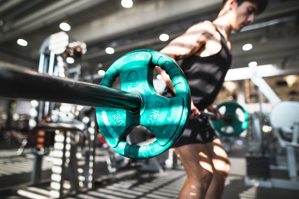 Young handsome fit man in gym working out, lifting bar of barbell, flexing muscles.