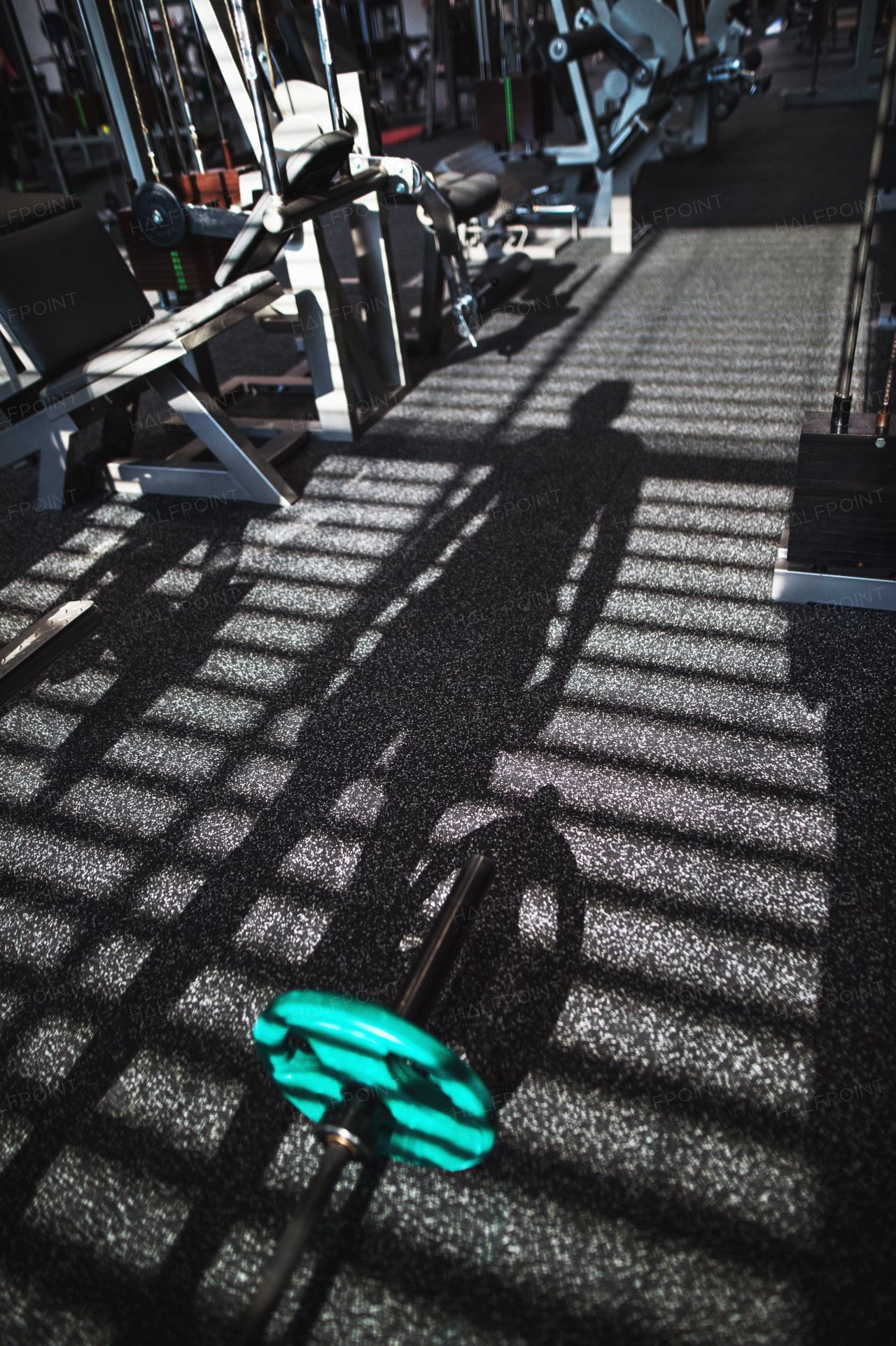 Modern gym with various exercise machines in it, a shadow of a person working out.