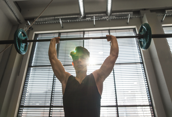 Young handsome fit man in gym working out, lifting bar of barbell, flexing muscles.