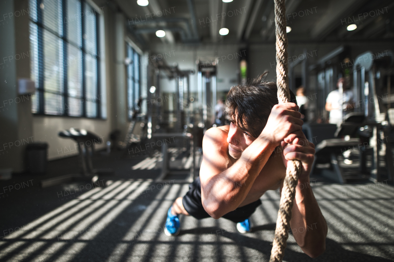 Young fit man working out in gym. A boy in a plank holding onto a climbing rope.