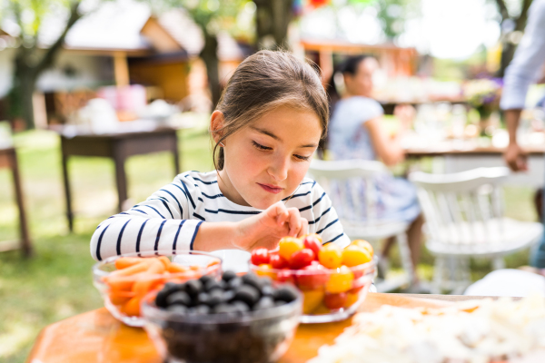 Family celebration outside in the backyard. Little girl standing at the table.