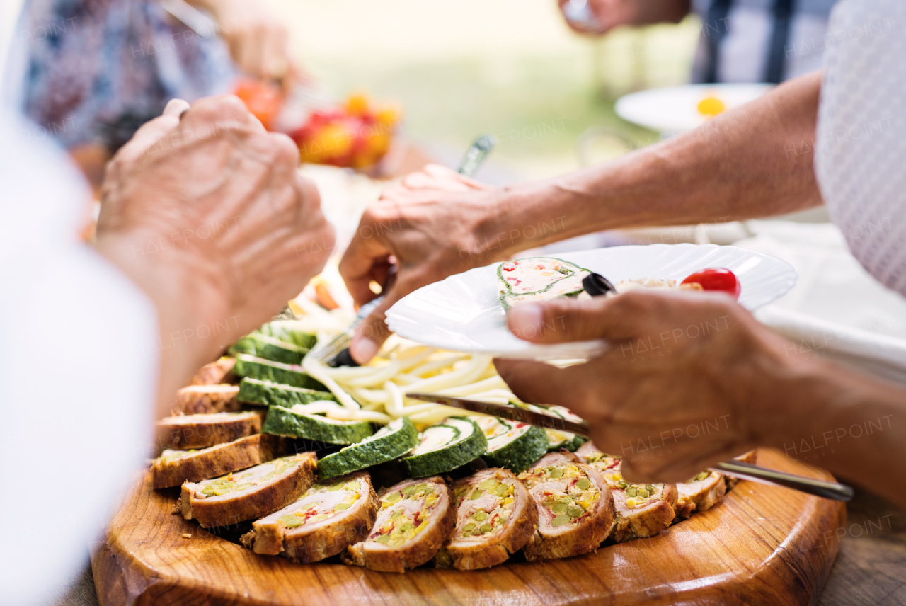 Close-up of unrecognizable people putting food on their plates. Family celebration outside in the backyard. Big garden party.