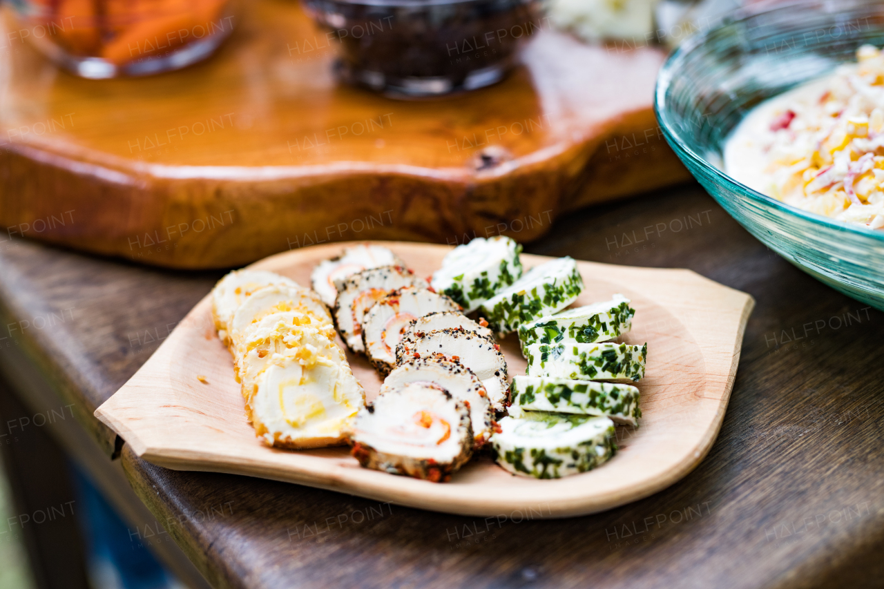 Close up of a table set for a garden party or celebration outside. Herby cheese roulade on a wooden serving bowl.