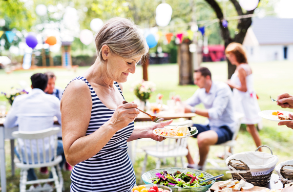 A senior woman putting food on her plate. Family celebration outside in the backyard. Big garden party.