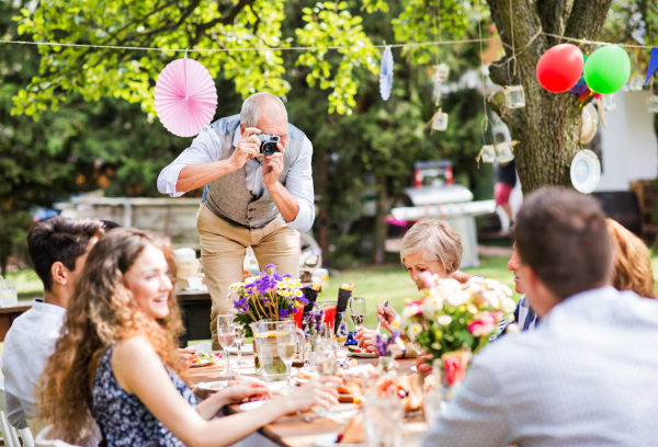 Family celebration outside in the backyard. Big garden party. Grandfather taking photo with a camera.