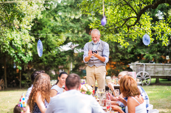 Family celebration outside in the backyard. Big garden party. Grandfather taking photo with a camera.