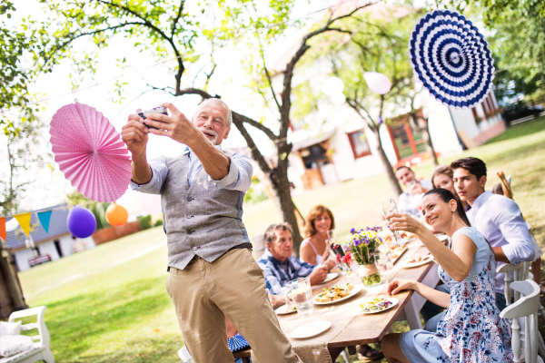 Family celebration outside in the backyard. Big garden party. A senior man taking selfie with a camera.