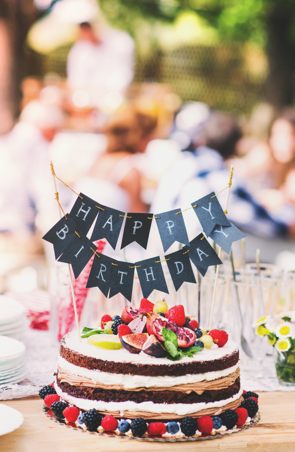 Family celebration outside in the backyard. Big garden party. Birthday party. Close up of a fruit birthday cake.