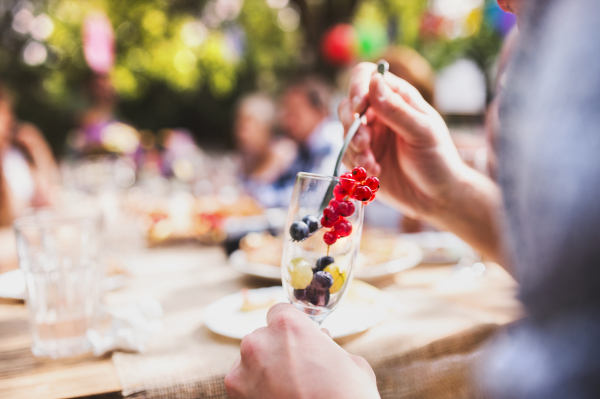 Family celebration outside in the backyard. Big garden party. Unrecognizable man eating fruit.