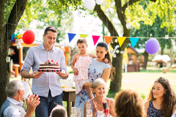 Family celebration outside in the backyard. Big garden party. Birthday party. A young man holding a birthday cake.