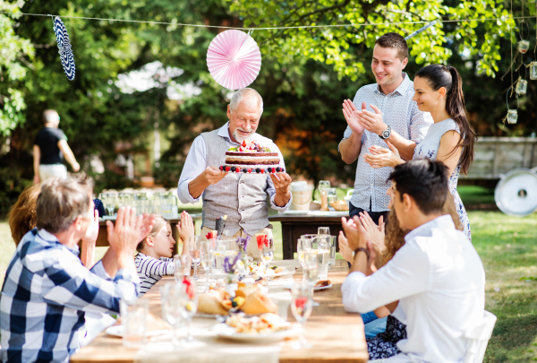 Family celebration outside in the backyard. Big garden party. Birthday party. A senior man holding a birthday cake.