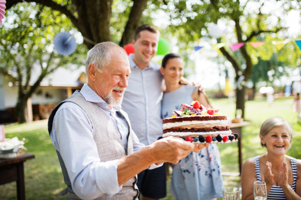 Family celebration outside in the backyard. Big garden party. Birthday party. A senior man holding a birthday cake.