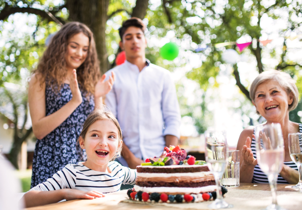 Family celebration outside in the backyard. Big garden party. Birthday party. Small girl with a birthday cake.