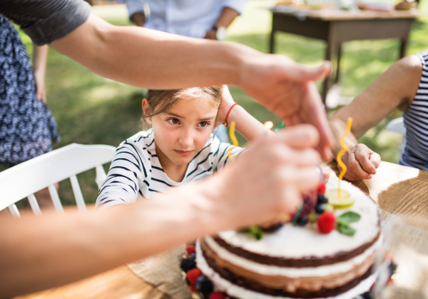 Family celebration outside in the backyard. Big garden party. Birthday party. Small girl with a birthday cake.