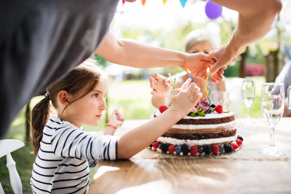 Family celebration outside in the backyard. Big garden party. Birthday party. Small girl with a birthday cake.