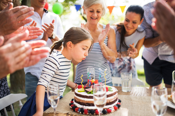 Family celebration outside in the backyard. Big garden party. Birthday party. Small girl with a birthday cake.