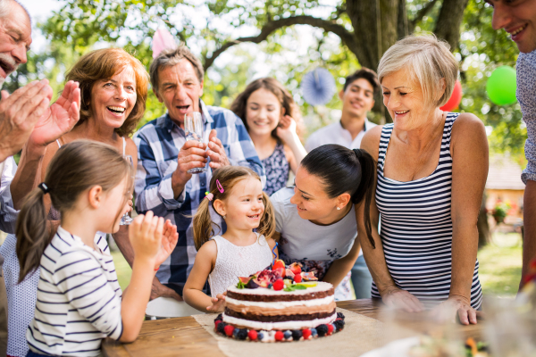 Family celebration outside in the backyard. Big garden or a birthday party. A small girl with a cake.