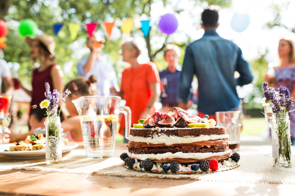 Family celebration outside in the backyard. Big garden party. Birthday party. Close up of a fruit birthday cake.