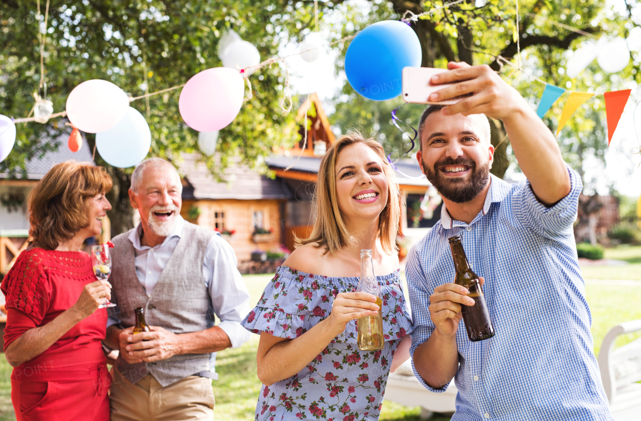 Happy young couple taking selfie at a party outside in the backyard, laughing.