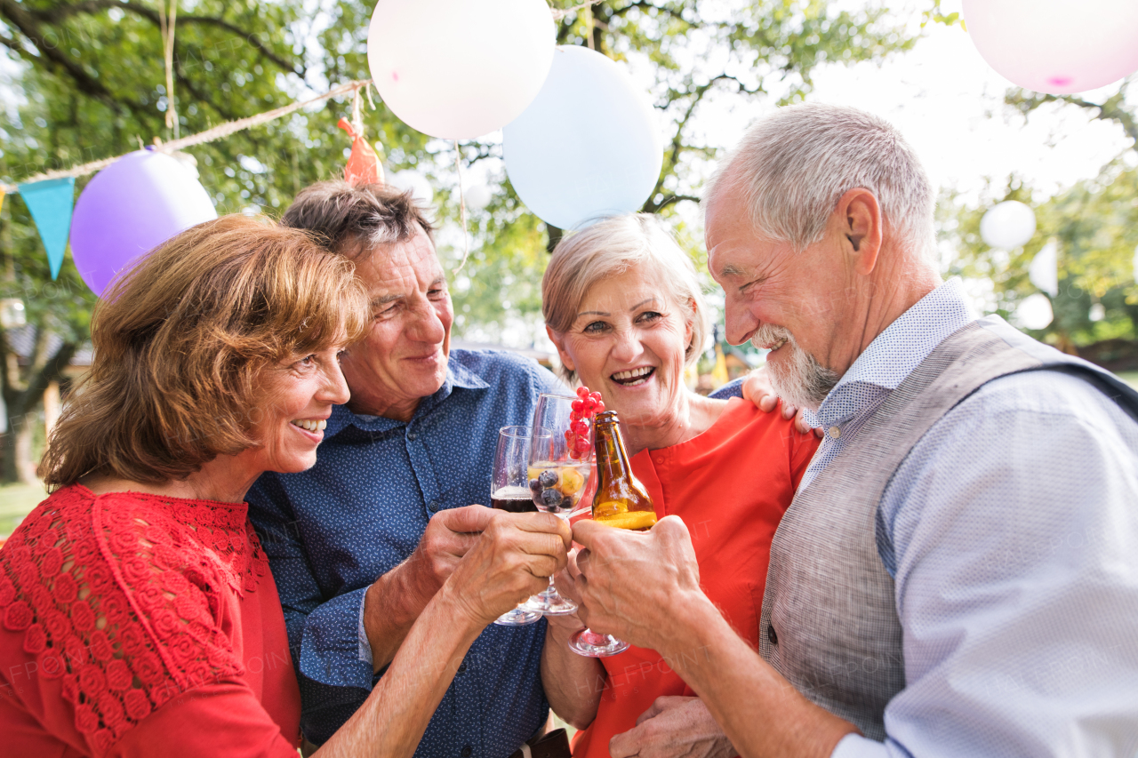 Family celebration outside in the backyard. Big garden party. Two senior couples clinking glasses and bottles.