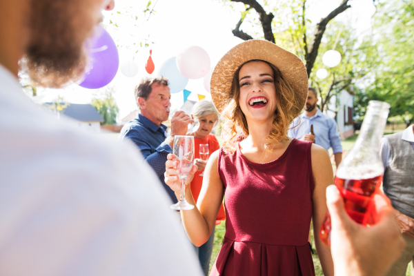 Young woman with hat holding a glass on a family celebration outside in the backyard. Barbecue party.