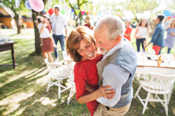 A senior couple dancing on a garden party or family celebration outside in the backyard.