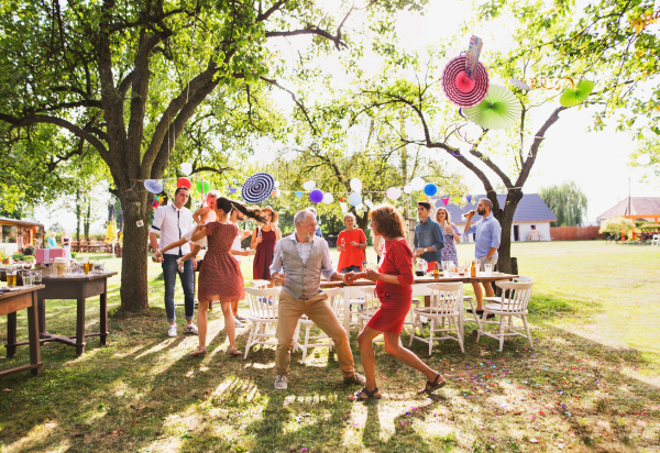 A senior couple with extended family dancing on a garden party or family celebration outside in the backyard.