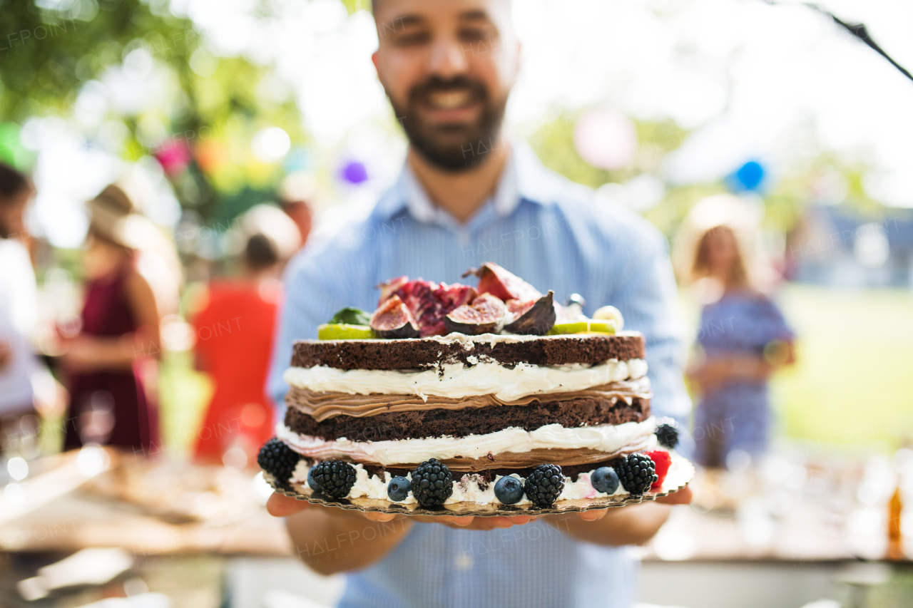 Family celebration outside in the backyard. Big garden or birthday party. Mature man with a birthday cake.