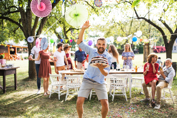 Family celebration outside in the backyard. Big garden or birthday party. Mature man holding a birthday cake.