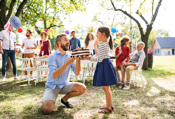 Family celebration outside in the backyard. Father giving a cake to a small girl on a birthday party.