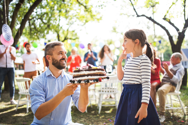 Family celebration outside in the backyard. Father giving a cake to a small girl on a birthday party.