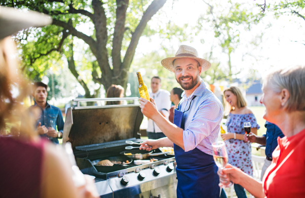 A mature man with family and friends cooking and serving food on a barbecue party outside. Family celebration in the backyard.