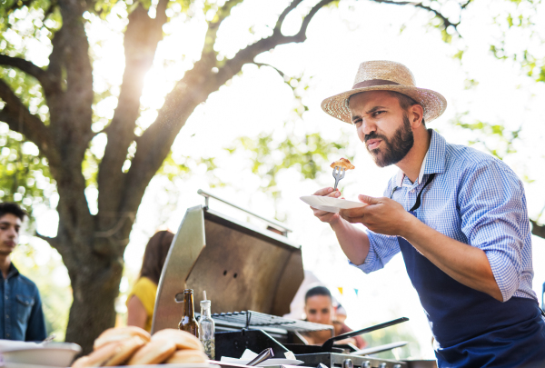 A mature man with family and friends cooking and serving food on a barbecue party outside. Family celebration in the backyard.