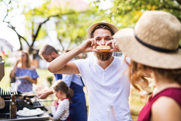 Family celebration outside in the backyard. Barbecue party. A young man eating hamburger.