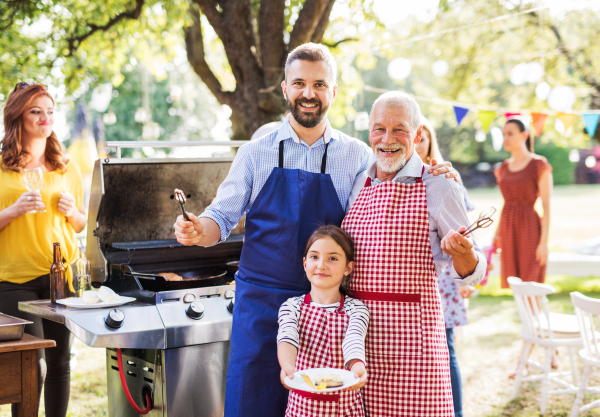 A mature man with family and friends cooking food on a barbecue party outside. Family celebration in the backyard.