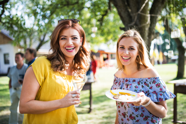 Portrait of women holding a glass of wine and a plate with grilled vegetables. A family celebration outside in the backyard. Barbecue party.