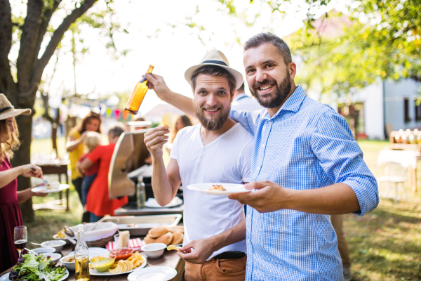 Portrait of men holding a bottle of beer and a plate with food. A family celebration outside in the backyard. Barbecue party.