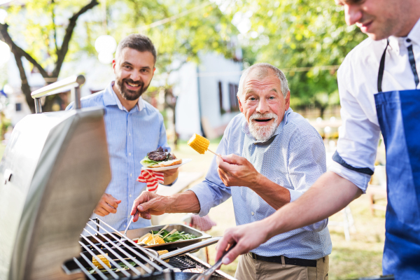 Men with family and friends cooking food on a barbecue party outside. Family celebration in the backyard.