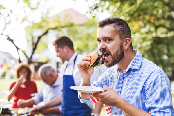 A mature man with family and friends cooking food on a barbecue party outside. Family celebration in the backyard.