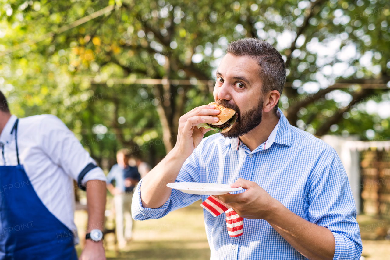 Family celebration outside in the backyard. Barbecue party. A mature man eating hamburger.