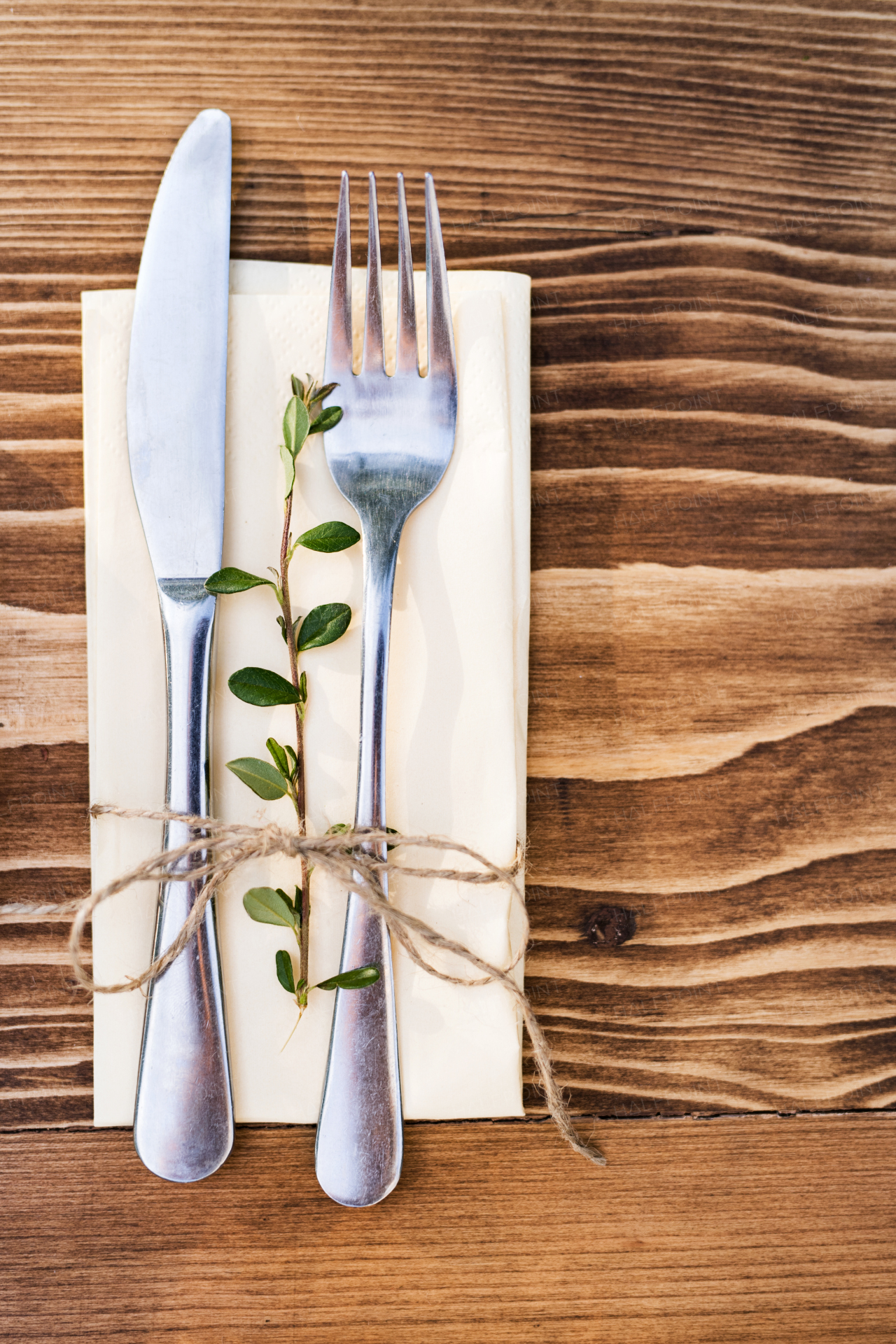 A knife and fork on a cream serviette laid on a brown, wooden table. Top view.