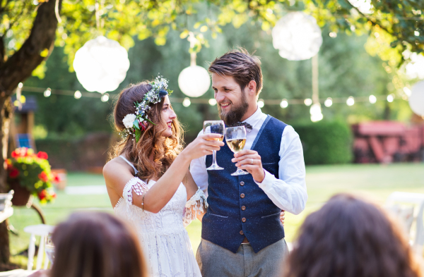 Wedding reception outside in the backyard. Bride and groom clinking glasses.