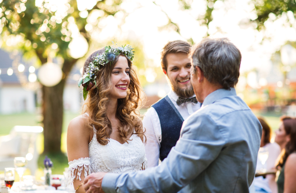 A senior father congratulating bride and groom at wedding reception outside in the backyard.