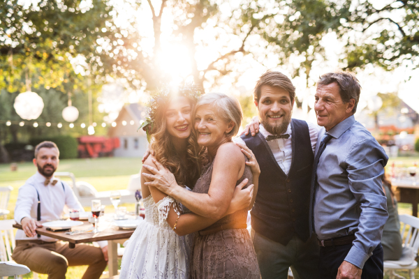 Wedding reception outside in the backyard. Family celebration. Bride, groom with parents posing for the photo at sunset.