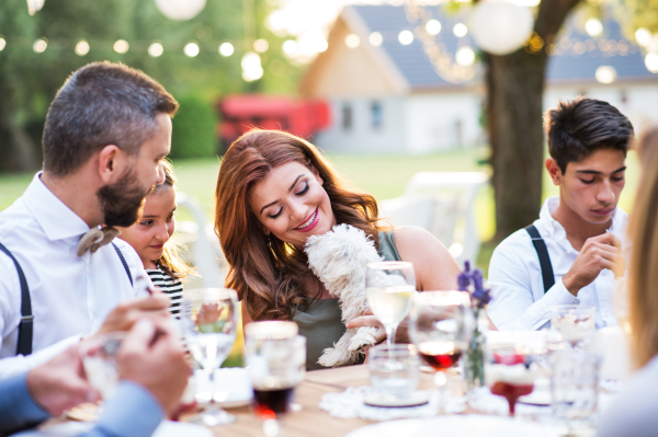 Guests with a small white dog sitting at the table outside in the backyard.