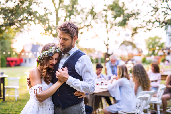 Wedding reception outside in the backyard. Bride and groom with a family dancing.